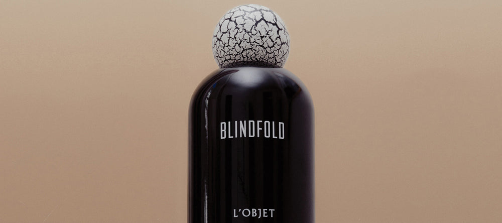Black perfume bottle with cracked cap labeled 'Blindfold' on a beige background