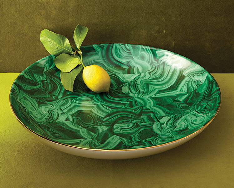 Green marbled dish with a lemon and leaves on a green surface