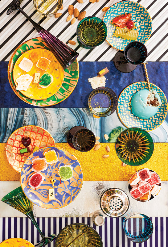 Collage of colorful tableware including plates, bowls, and glasses on a striped background.