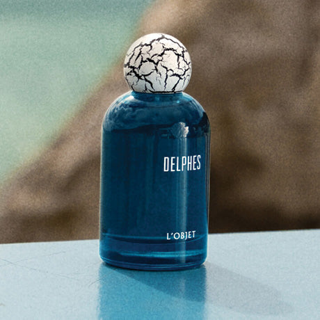 Blue fragrance bottle with white crackled top in beach setting