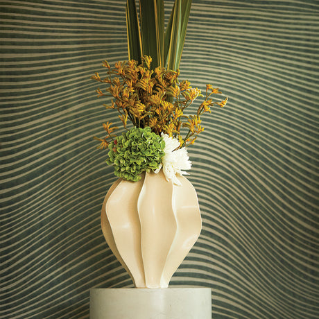 Decorative vase with flowers against a wavy green and beige wall.