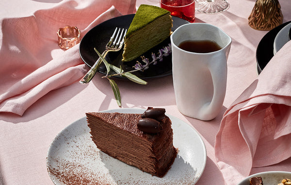 Tabletop with cake slices on iron and stone glazed Terra dessert plates, stone Timna mug, pink table linens.
