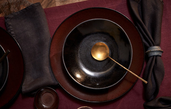 Iron and wine glazed Terra plate stack, gold spoon, Burgundy tablecloth, black linen napkins and iron porcelain napkin rings.
