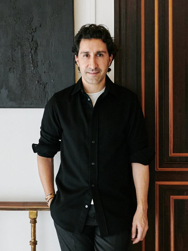 Man in a black shirt standing in front of a wooden door with decorative elements.