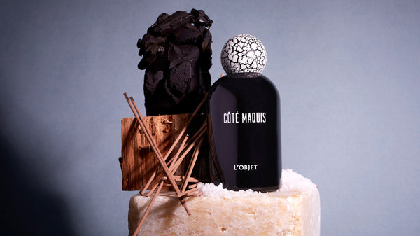 Cote Maquis Black Porcelain Fragrance Bottle with White Crackle Wooden Top arranged on top of a white stone with salt, incense, wooden objects in front of a grey textured background.