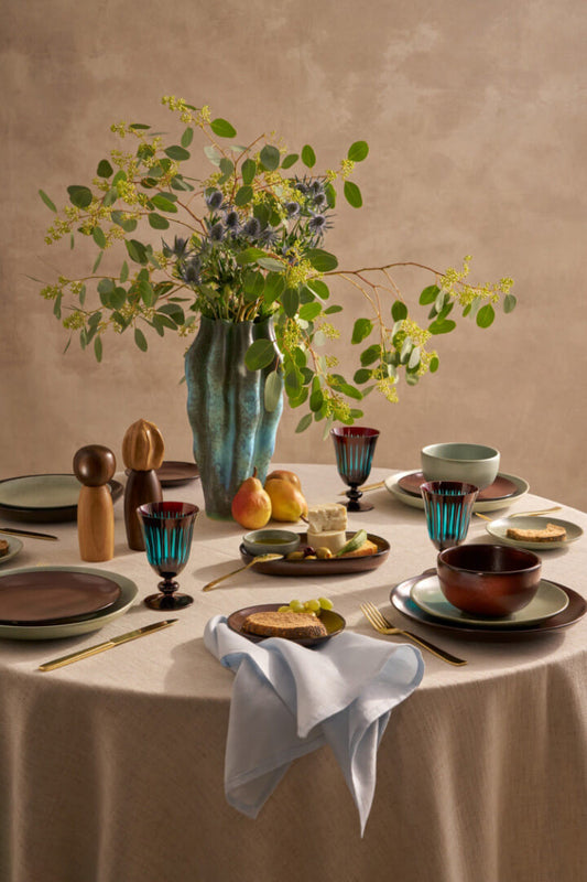 Dining table set with ceramic plates, bowls, and glasses, accompanied by a vase of flowers.