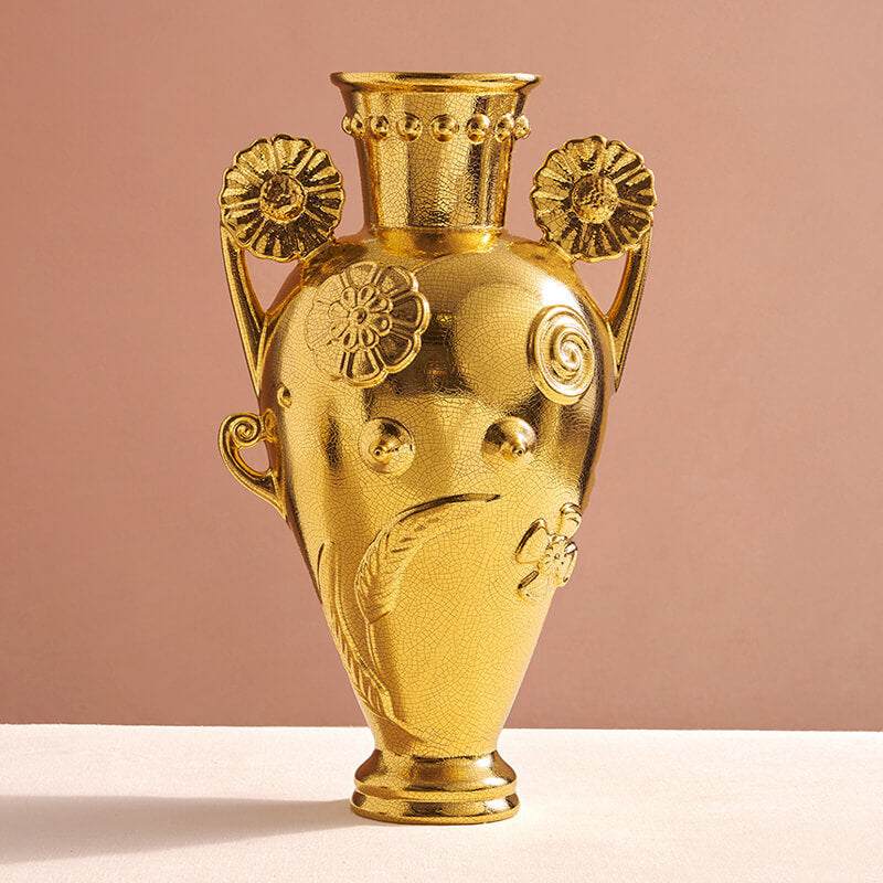 Decorative gold vase with intricate designs on a pink background