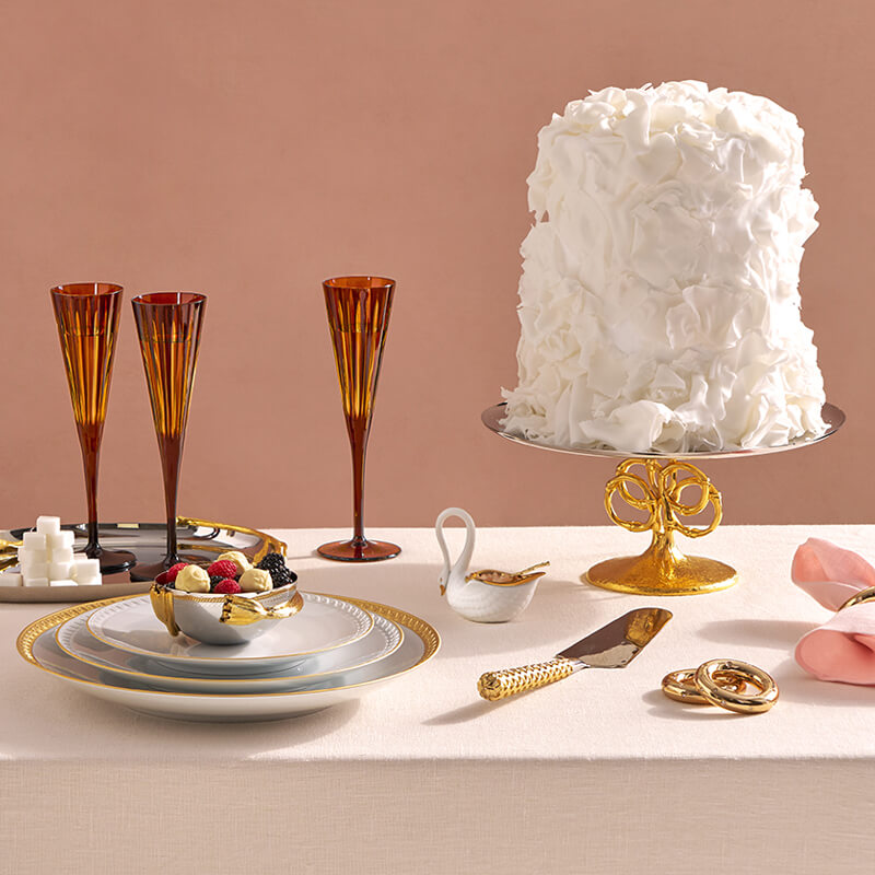 Table setting with a white cake, glasses, plates, and cutlery on a beige background