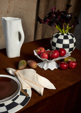 Tabletop with Damier round vase and placemat with black and white checkerboard pattern, white shell-shaped Neptune bowl, Timna pitcher with stone glaze